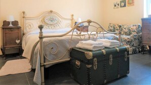 A bedroom with a bed, a nightstand, a floral armchair, and a vintage suitcase. - The Best Place To Visit Como Lake (Barni (COMO))
