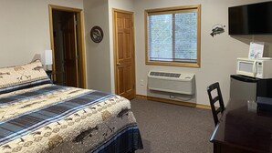 Une chambre à coucher avec un lit, un bureau, une télévision, une fenêtre et une porte.