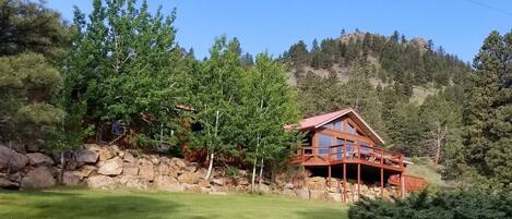 A cabin with a red roof, wooden deck, and a stone wall.