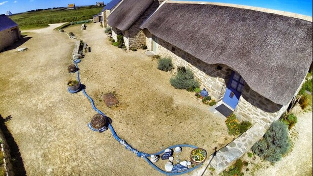 A rural property with stone buildings, a gravel driveway, and a thatched-roof house.