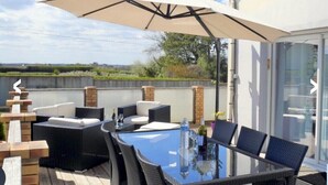 An outdoor patio with a glass table, wicker furniture, and a large umbrella.