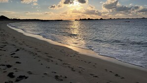 A beach with footprints leading to the water, a clear sky, and distant landforms.