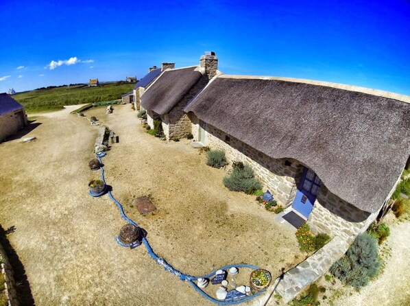 Une propriété rurale avec des bâtiments en pierre, une allée gravillonnée et une maison à toit de chaume.