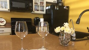 A kitchen counter with two wine glasses, a vase with flowers, a corkscrew, and a note.