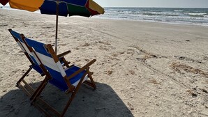 A beach scene with a wooden beach chair and a colorful umbrella under bright sunlight.