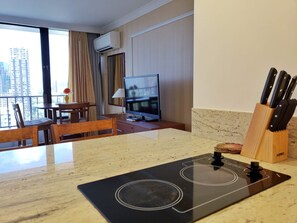 Cozinha moderna com fogão embutido, área de refeições com mesa e cadeiras, televisão e vista para a cidade.