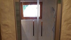 A glass-enclosed shower area with a visible window and a showerhead. - Atypical Cottage in the Chapel of the Miners (Sainte-Marie-Aux-Mines)
