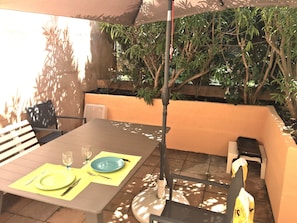 Enjoy a romantic meal under the shade of a large umbrella, surrounded by lush greenery and a low wall.