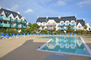 Ein Swimmingpool mit blauen Liegestühlen und einem Gebäude mit Balkonen.