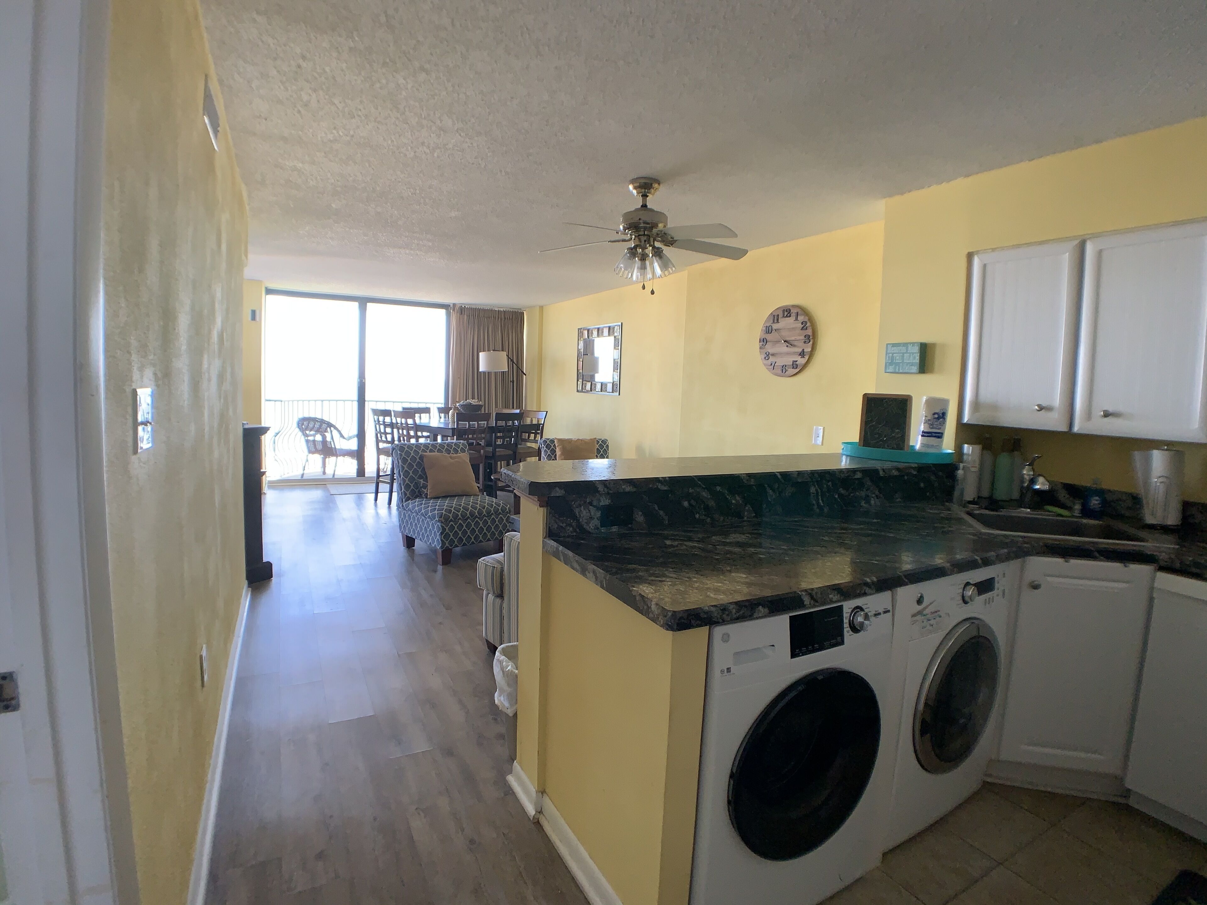 A compact kitchen with a washing machine, a dining area with chairs, and a ceiling fan.