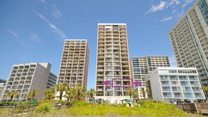 A high-rise hotel with multiple floors, balconies, and a central courtyard with palm trees. - Amazing Views - Ocean Front 3BR Condo! (Myrtle Beach)