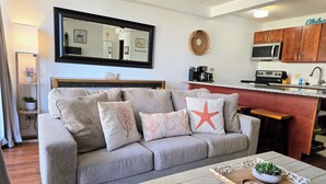 Un salon comprenant un canapé, une table basse avec un plateau, un coin cuisine équipé d’un four à micro-ondes et un bar pour prendre les repas.