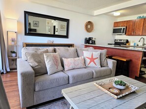 Een woonkamer met een bank, een salontafel met een dienblad, een keukenhoek met een magnetron en een eettafel.