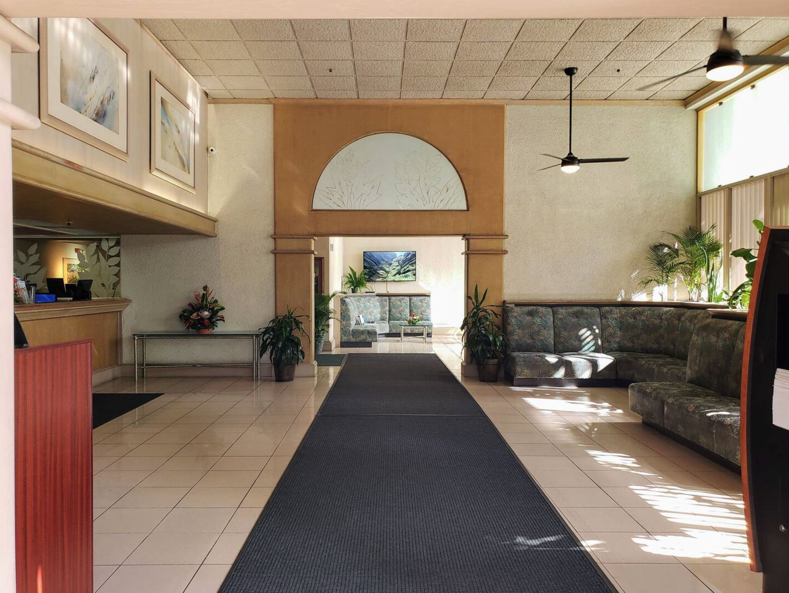 A hotel lobby with a reception desk, a black carpeted walkway, a sofa, and a large arched window.
