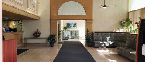A hotel lobby with a reception desk, a black carpeted walkway, a sofa, and a large arched window.