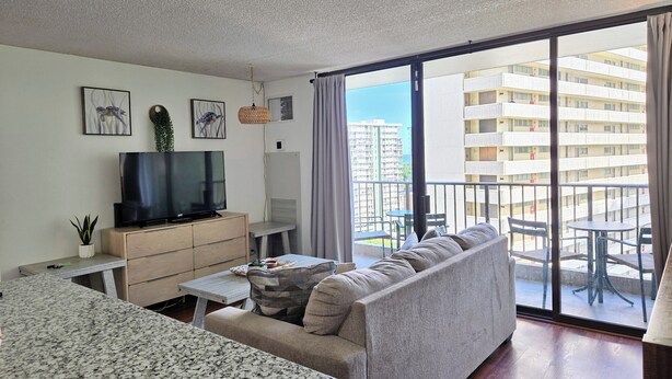 Un salon moderne avec un canapé, un téléviseur et une table à manger, ainsi qu’un balcon offrant une vue sur les immeubles de grande hauteur.