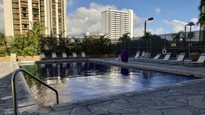 Une piscine dotée de chaises longues et d’une terrasse en pierre, entourée de grands immeubles et de palmiers.