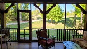 A covered porch with a wooden floor, a red chair, a striped sofa, and a view of a golf course.
