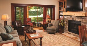 Un salon chaleureux avec une cheminée, des fauteuils confortables, un téléviseur et une grande fenêtre donnant sur l’extérieur.