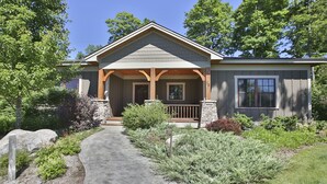 A two-story house with a covered porch, stone pillars, and a stone pathway leading to the entrance.