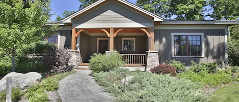 A two-story house with a covered porch, stone pillars, and a stone pathway leading to the entrance.