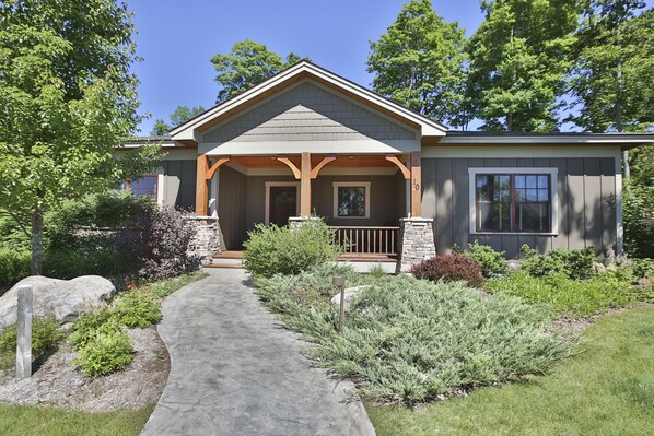 A two-story house with a covered porch, stone pillars, and a stone pathway leading to the entrance.