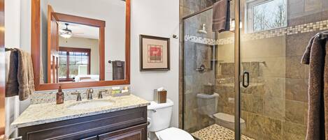 Un baño con cabina de ducha de vidrio, un lavamanos con tocador y un inodoro.
