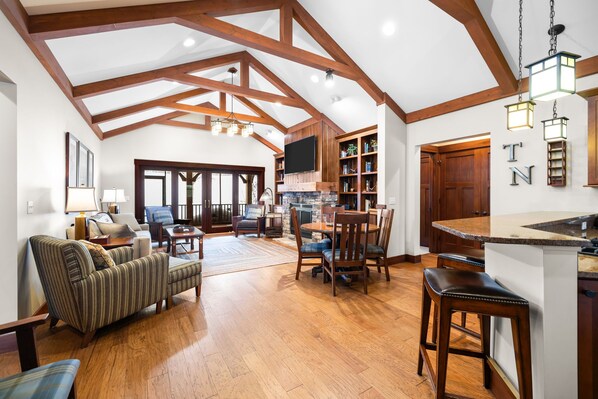 A spacious living area with a high ceiling, wooden beams, a fireplace, and a dining area with a kitchen counter.