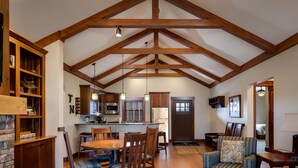A spacious living area with a high ceiling, wooden beams, a dining table with chairs, a sofa, and a kitchen area with modern appliances.