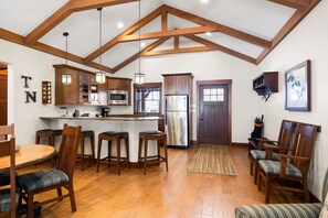 A kitchen with wooden beams, a central island, bar stools, and a dining table with chairs.