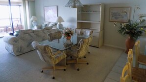 A living room with a glass-top dining table, four chairs, a sofa, a bookshelf, and a hanging lamp. - Gateway to Sanibel/Captiva 2/2 Ft. Myers Condo (Ft Myers)