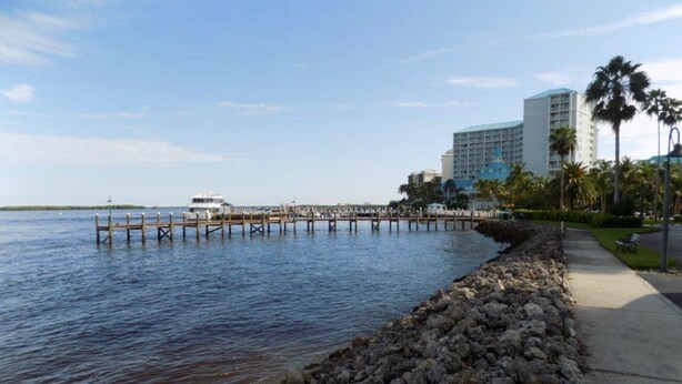 A waterfront hotel with a dock extending into the water, a rocky shoreline, and a clear sky. - Gateway to Sanibel/Captiva 2/2 Ft. Myers Condo (Ft Myers)