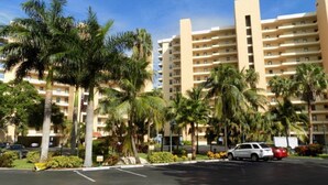 A multi-story hotel with a parking lot, palm trees, and a clear blue sky. - Gateway to Sanibel/Captiva 2/2 Ft. Myers Condo (Ft Myers)