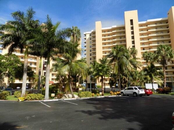 A multi-story hotel with a parking lot, palm trees, and a clear blue sky.