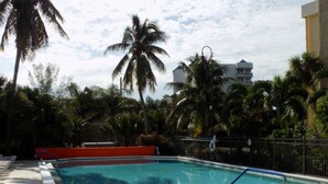 A swimming pool with a tiled deck, surrounded by palm trees and a fence. - Gateway to Sanibel/Captiva 2/2 Ft. Myers Condo (Ft Myers)