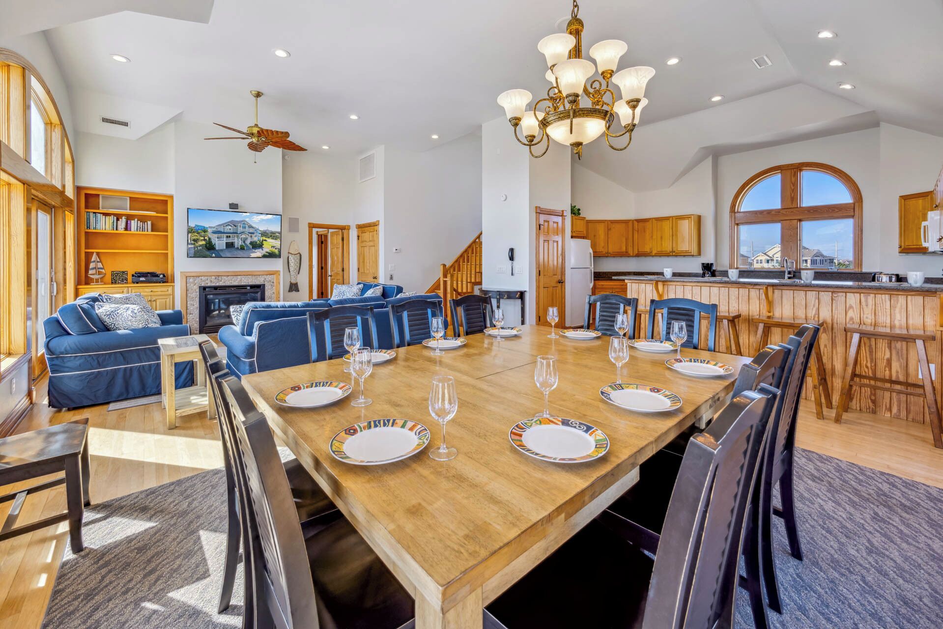 A spacious living room with a large wooden dining table set for six, blue sofas, and a fireplace.