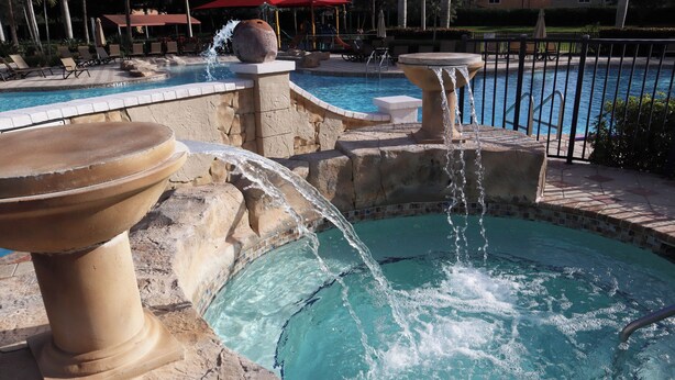 Ein Poolbereich mit Wasserspiel, Liegestühlen und einer Steinmauer.