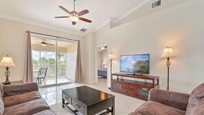 Ein geräumiges Wohnzimmer mit einem Flachbildfernseher, zwei Sofas, einem Couchtisch und einem Deckenventilator.