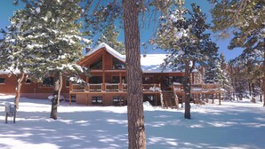 A log cabin with a balcony and a deck, surrounded by snow-covered trees.