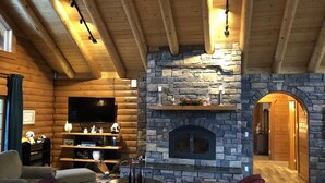 A cozy log cabin interior with a stone fireplace, wooden beams, a television, and a seating area.