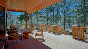 A wooden deck with outdoor furniture, overlooking a forested area.