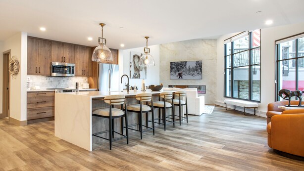 A modern kitchen with a central island, bar stools, and a seating area with a bench and orange sofa. - Vail Center Place | Unit 2 - 2 Bedroom Diamond (Vail)
