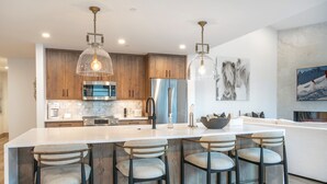 A modern kitchen with wooden cabinets, stainless steel appliances, and a large island with bar stools. - Vail Center Place | Unit 2 - 2 Bedroom Diamond (Vail)