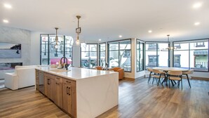 A modern kitchen with a large island, wooden cabinets, and a dining area with a round table and chairs. - Vail Center Place | Unit 2 - 2 Bedroom Diamond (Vail)