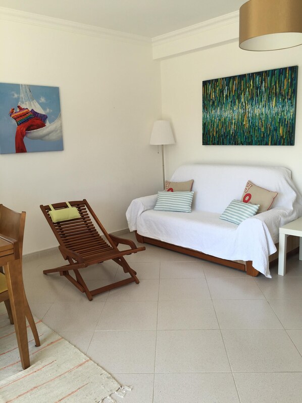A living room with a wooden chair, a white sofa, a lamp, and two paintings on the walls. - BEAUTIFUL APARTMENT A FEW STEPS FROM THE SEA AND IN A VERY PRETTY FISHING VILLAG (Cabanas da Tavira)