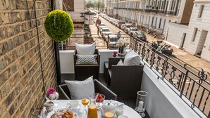Un coin repas avec une table mise pour le petit-déjeuner, comprenant des croissants, des fruits et des boissons, donnant sur une rue de la ville.