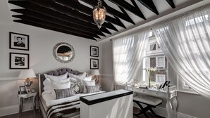 Une chambre à coucher comprenant un lit, des tables de chevet, un bureau et une fenêtre avec des rideaux légers.