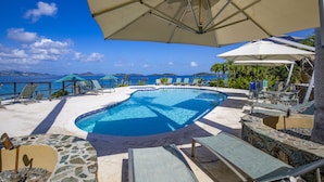 Une piscine dotée de chaises longues et de parasols, offrant une vue sur un plan d’eau et des montagnes.