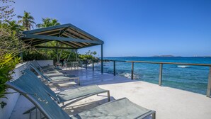 Un salon de plage doté de chaises longues et d’un espace de détente couvert, offrant une vue sur l’océan.