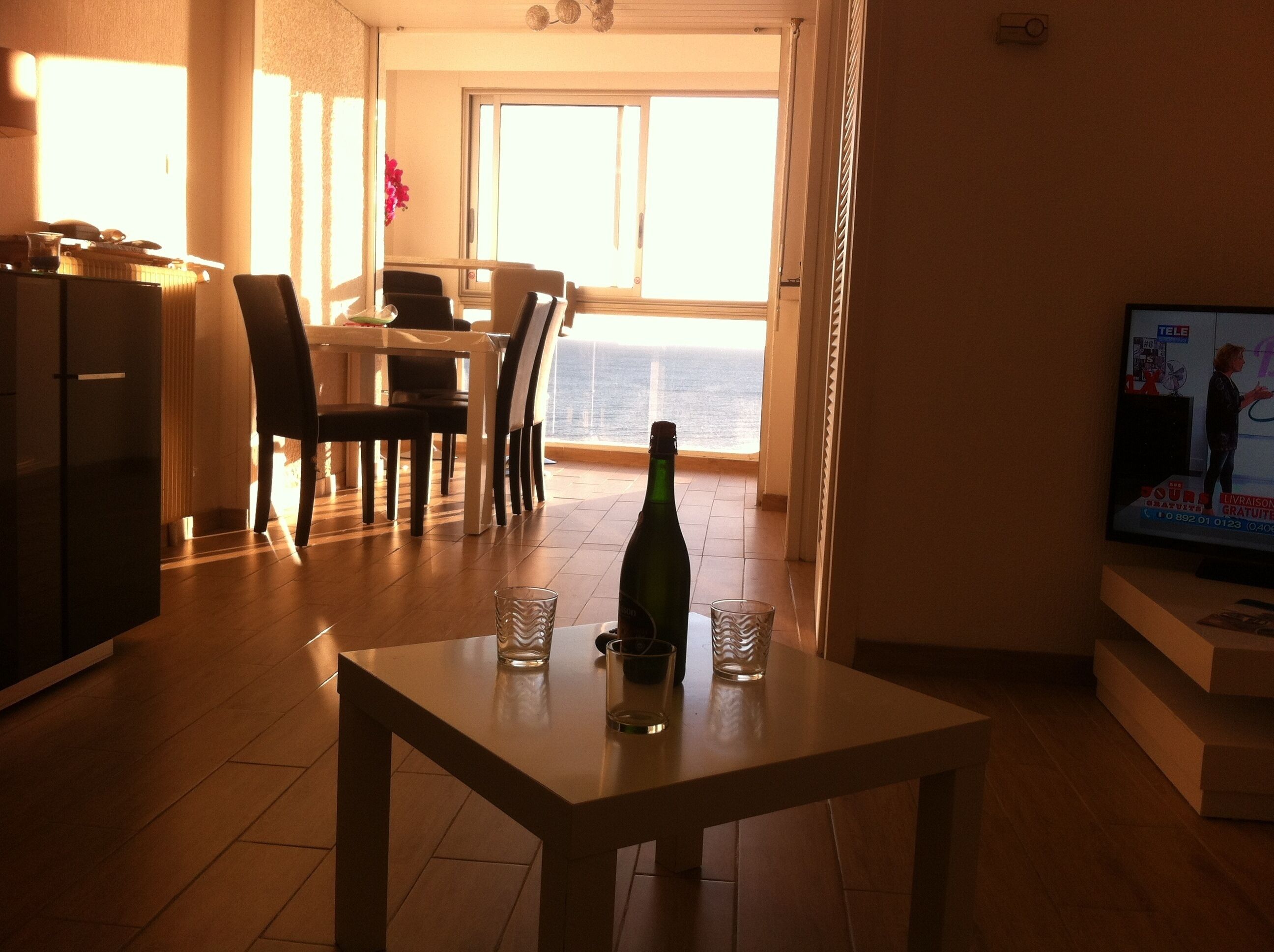 A living room with a dining area, a TV, and a bottle of champagne on a table.